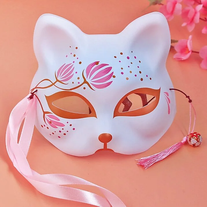 Masque japonais en forme de chat blanc avec motifs floraux roses et dorés, ruban rose attaché sur le côté