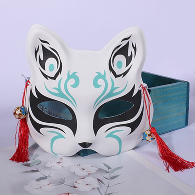 Masque japonais Kitsune l'Ingénieux blanc avec motifs noirs et turquoise, décoré de pompons rouges, vue de face