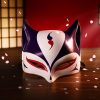 Masque japonais Kitsune élégant en plastique blanc avec motifs rouge et noir, forme de renard sacré, posé sur une table en bois avec des pétales de fleurs autour