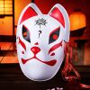 Masque japonais Kitsune Le Métamorphe blanc avec motifs rouges et noirs, décoré d'un symbole noir sur le front, rubans rouges attachés sur le côté