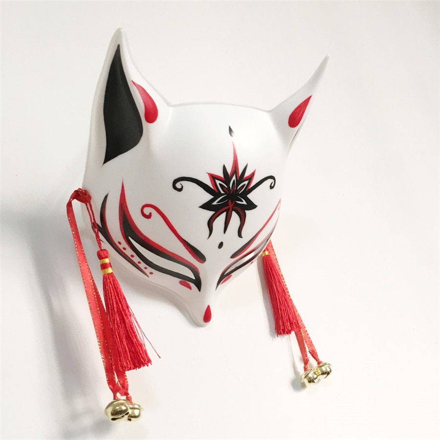 Masque japonais Kitsune Le Retord blanc en céramique avec motifs rouges et noirs, décor floral noir sur le front, pompons rouges et petites clochettes dorées