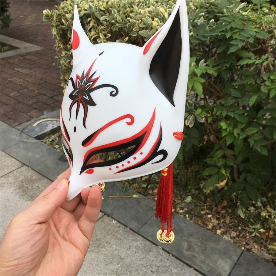 Masque japonais Kitsune Le Retord blanc en résine avec motifs rouges et noirs, détail d'oreilles pointues et pampilles rouges dorées
