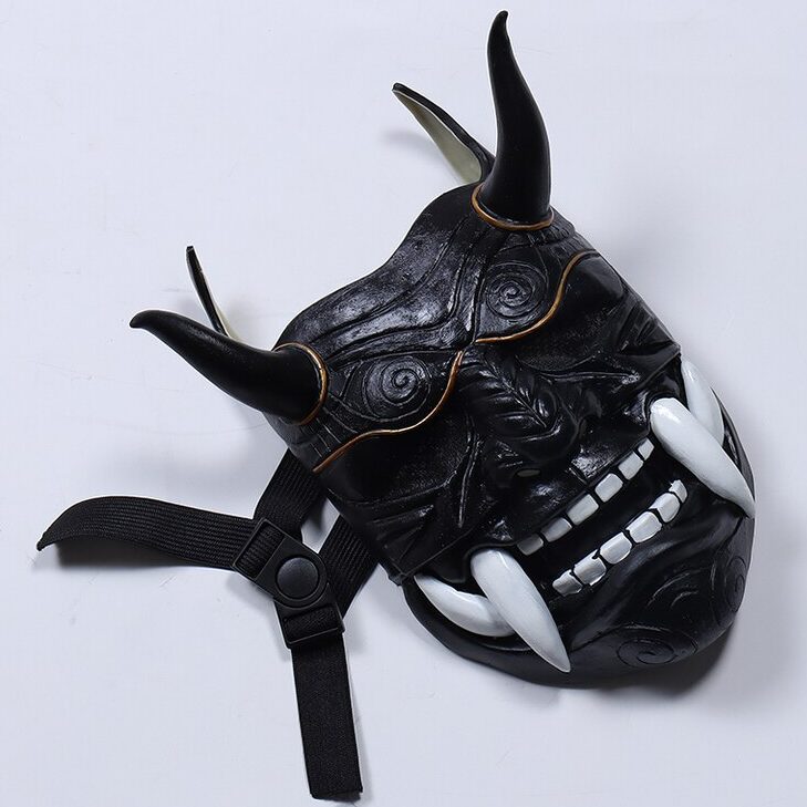 Masque japonais Oni noir en matière rigide avec cornes noires et défenses blanches, vue de face légèrement inclinée montrant les détails sculptés et la sangle réglable