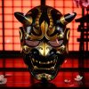 Masque japonais Oni noir et doré en résine avec détails dorés brillants et expression féroce, décor traditionnel japonais en arrière-plan
