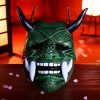 Masque japonais Oni vert en matière artisanale avec grandes défenses blanches et cornes noires brillantes, décor sculpté traditionnel